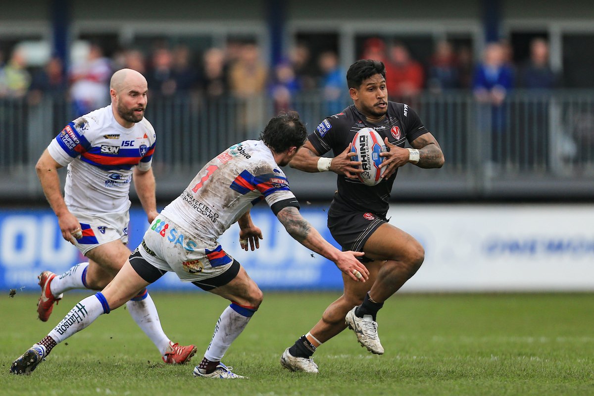 Ben Barba of St Helens, wearing a black change strip, runs past Scott Grix of Wakefield Trinity, while holding the ball.