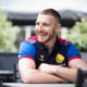 Jackson Hastings, formerly of Wigan Warriors and Salford Red Devils, looks to the side and smiles, in a navy Great Britain RL polo shirt.