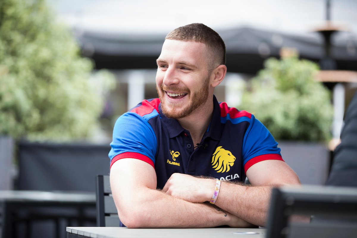 Jackson Hastings, formerly of Wigan Warriors and Salford Red Devils, looks to the side and smiles, in a navy Great Britain RL polo shirt.