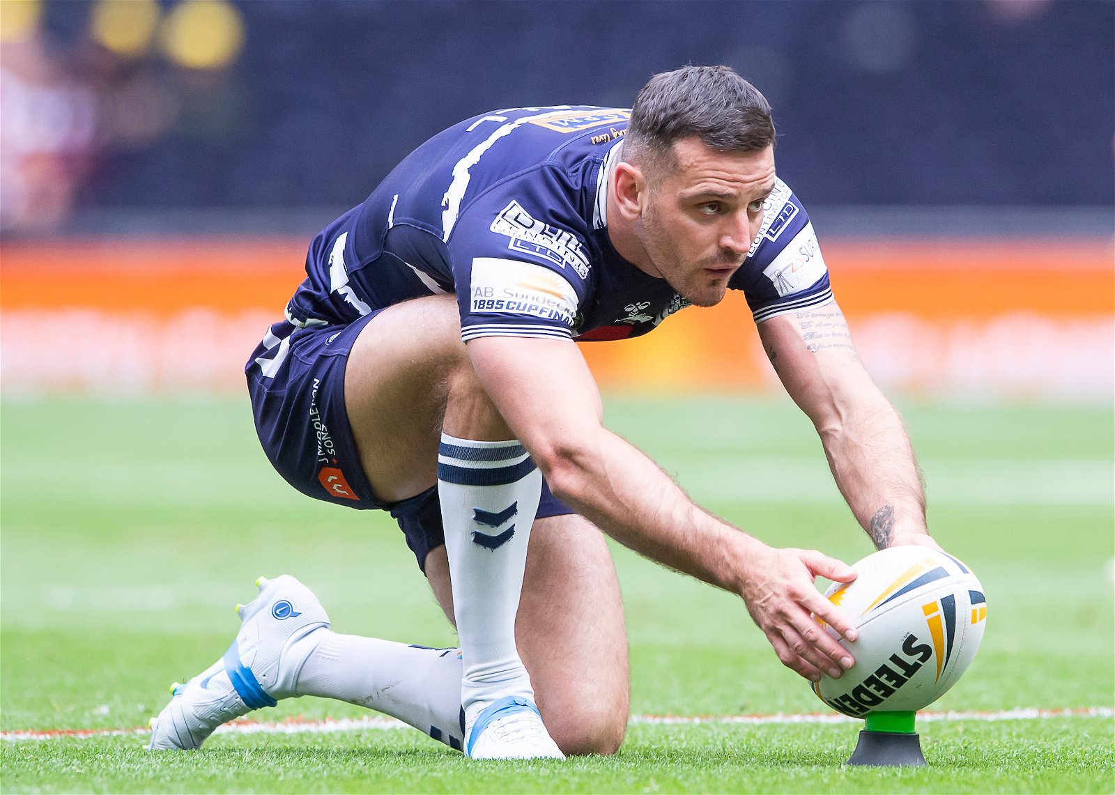 Craig Hall takes a kick for Featherstone Rovers. The ball is on the kicking tee and he leans down to position it, looking up.