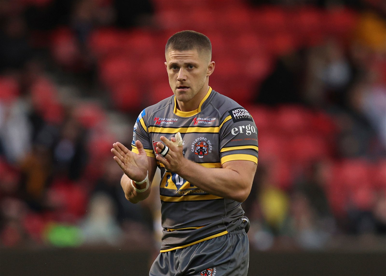 Ryan Hampshire claps while playing for Castleford Tigers, wearing a grey shirt with yellow horizontal pinstripes.