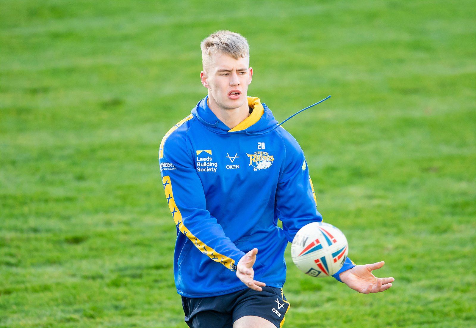 Max Simpson wearing a blue and yellow Leeds Rhinos hoodie while training. He is throwing the ball.