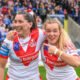 St Helens players Philippa Birchall and Faye Gaskin celebrating their sides victory over York, wearing traditional white shirts with a red V, standing on the pitch