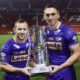 Rob Burrow and Kevin Sinfield hold the Super League trophy in the corner of an empty Old Trafford stadium.