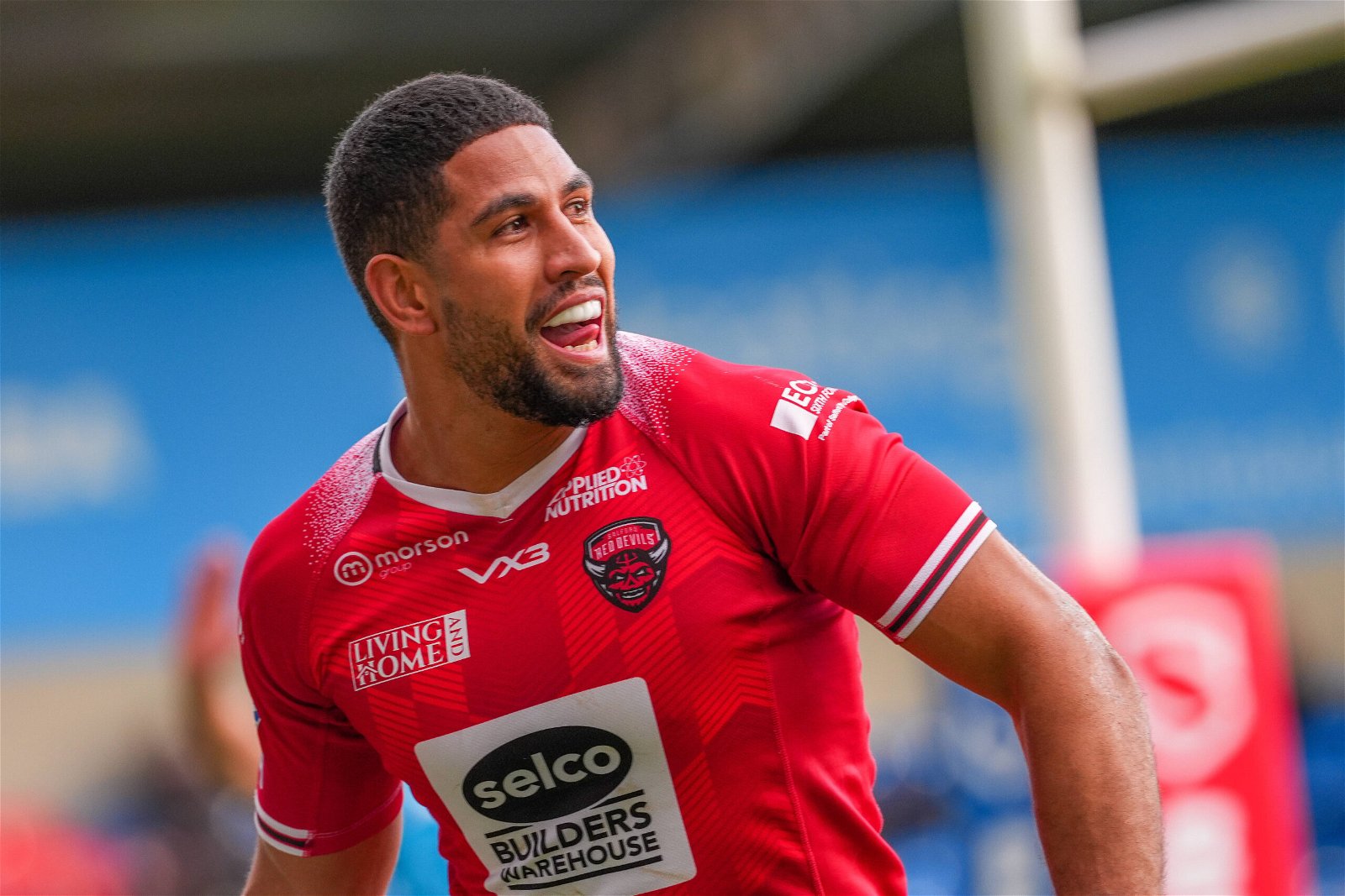 Nene Macdonald, while we're attempting to look at his shirt, celebrates a try.His shirt is red. There's a tiny gradient from white to red coming off the sides of the collar and I'm really sorry but I don't really know how else to describe it. The Selco logo is in a big white box. 
