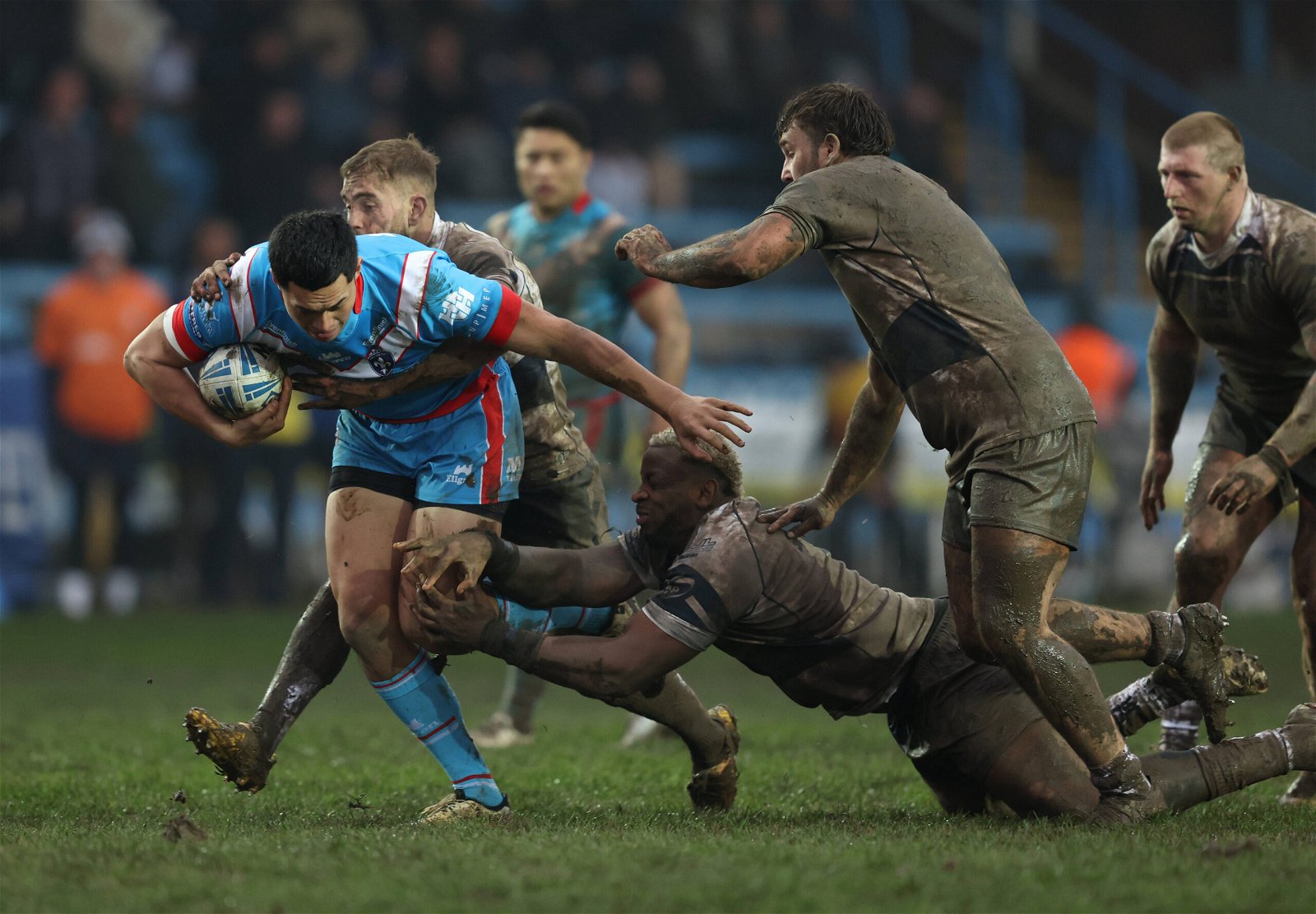 Wakefield Trinity player Isaiah Vagana in action with Featherstone Rovers' Gadwin Springer. They are covered in mud from head to toe.