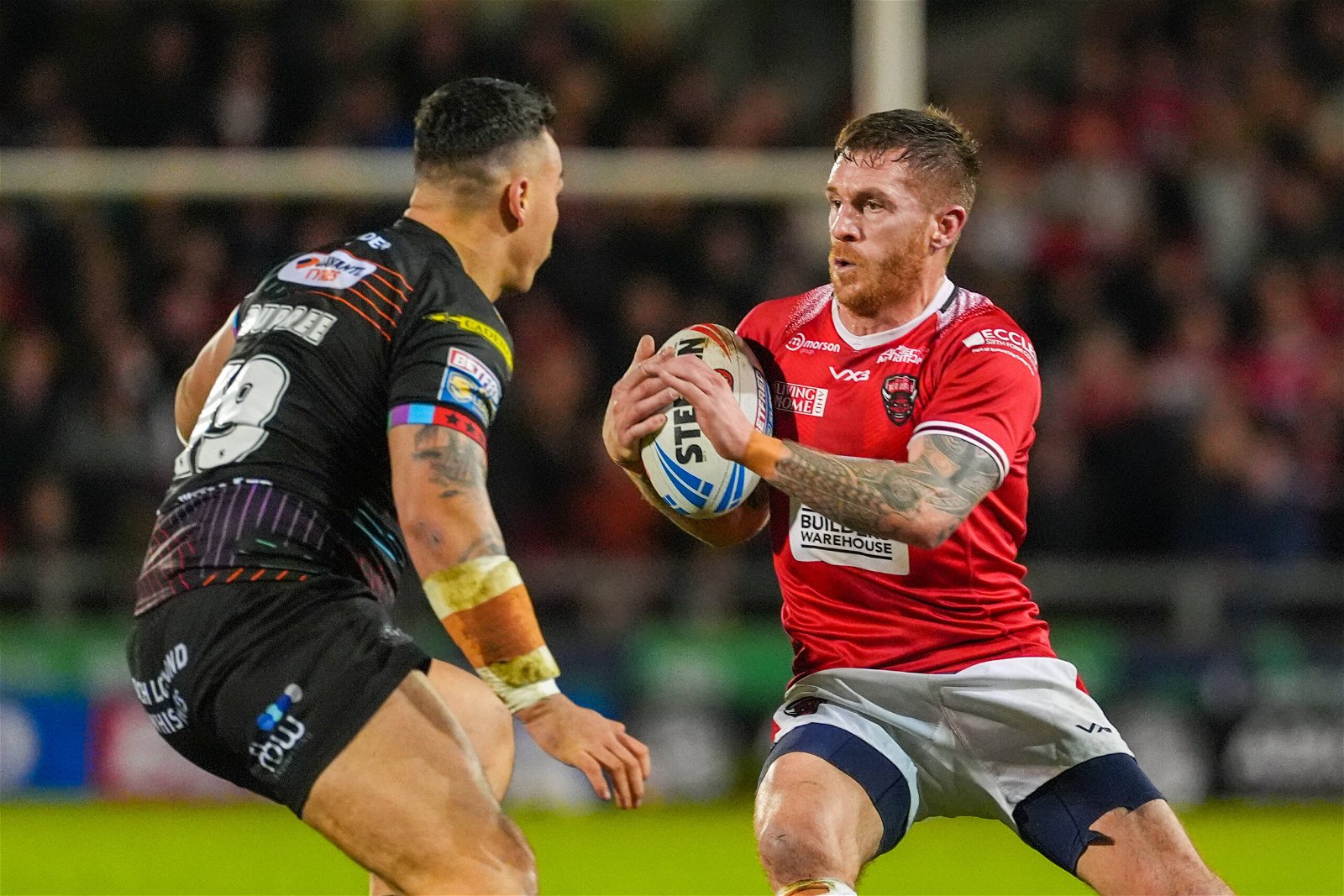 Marc Sneyd, playing for Salford, runs with ball in hand, looking to evade a defender. He leads the Man of Steel standings.