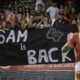 Sam Tomkins looks at a sign saying "Sam is back". Catalans Dragons